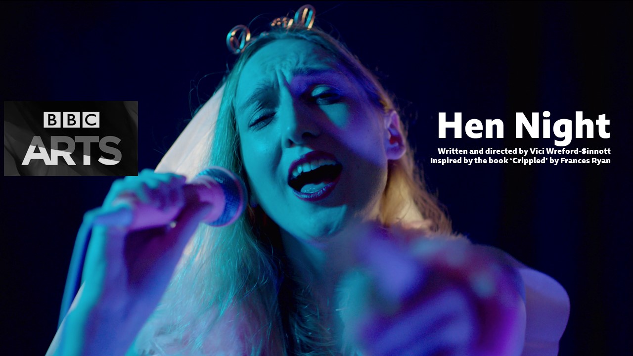 Image description - A film still from Hen Night, tinted with blue and purple hues. Nicola Chegwin plays Jessica, a young disabled white woman with long blond hair. In the image she is singing and pointing into camera, holding a microphone firmly in her hand. She is wearing hen party accessories including a white dress, feather boa, pink fluffly handcuffs and a costume white veil on a tiara which says 'bride' on it. The veil is over the back of her hair and not her face. She is wearing a hen party sash.